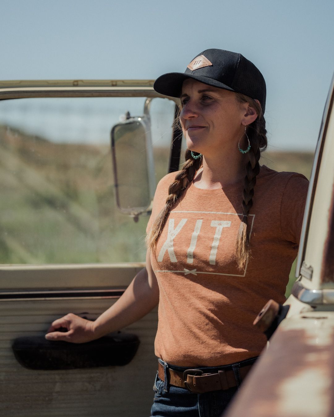 Photo of co-ranch manager Tiffany Lard wearing a black XIT logo ball cap and a orange XIT logo shirt, stepping out of an old rusty truck