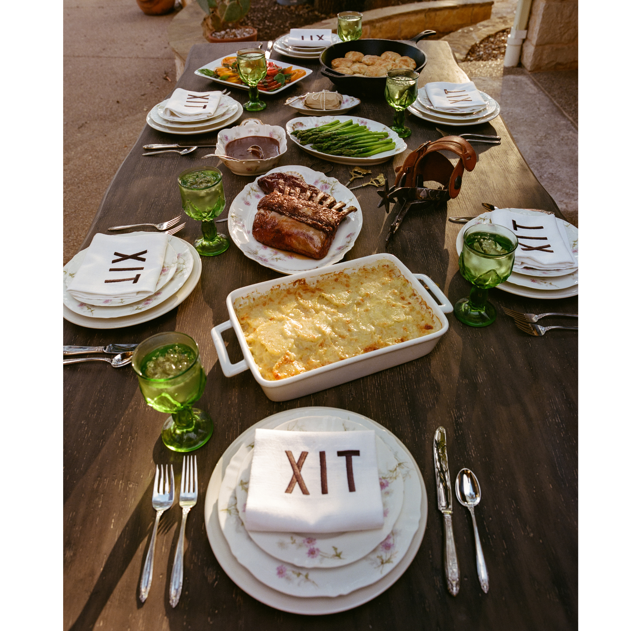A dinner table: biscuits, asparagus, ribs, gravy and mashed potatoes. Set: green goblets, silver cutlery, white china plates with XIT logo napkins