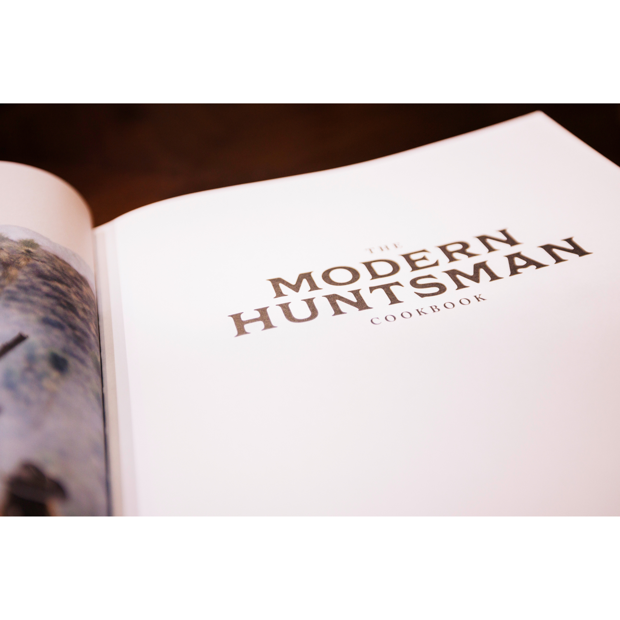 Open cookbook titled 'The Modern Huntsman Cookbook' on a wooden surface.