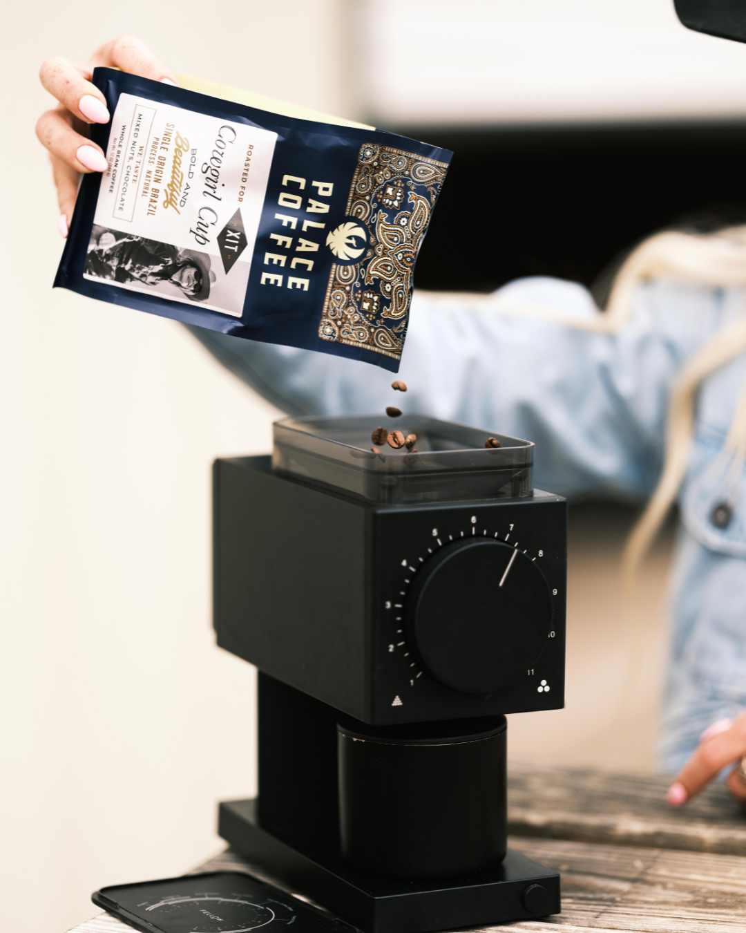 Person holding a Palace Coffee package above a black coffee grinder.