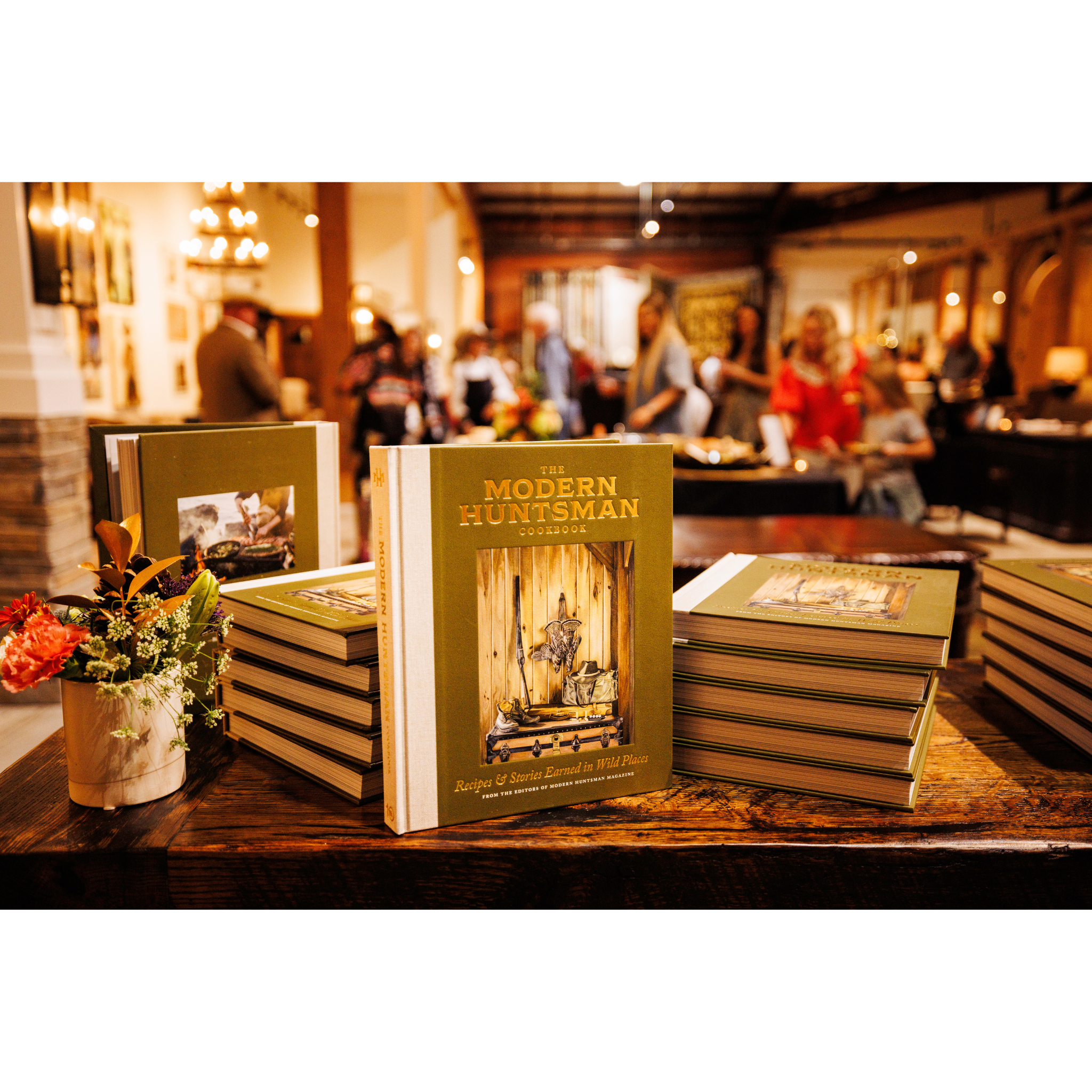 Stack of books titled 'The Modern Huntsman' on a wooden table with a blurred background of people.
